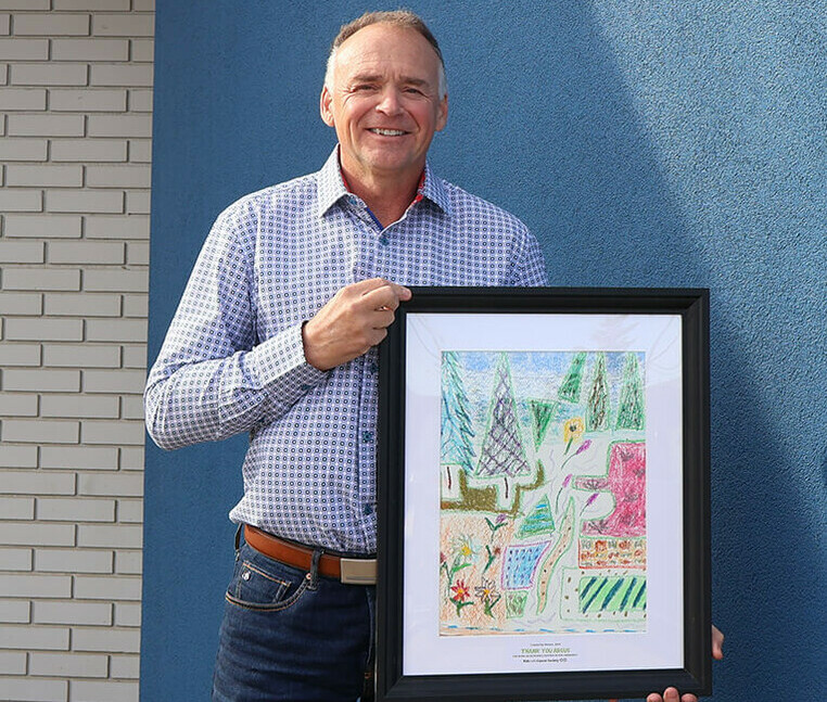 Argus CEO, Dwayne Sample, pictured holding the artwork created by Roman, one of the children who has been supported by Kids with Cancer.